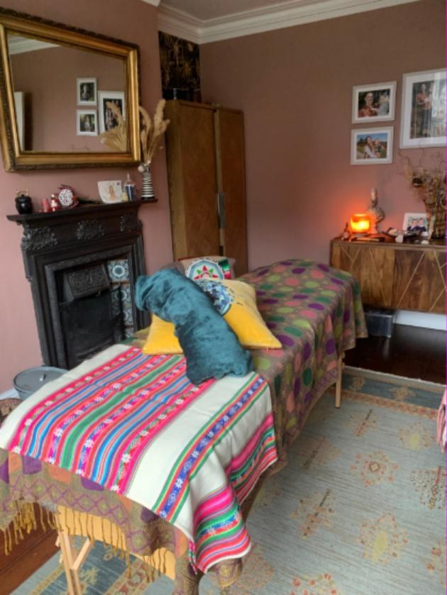 The healing space set up for a session, with candles, framed photographs and soft lamplight beside the treatment couch.