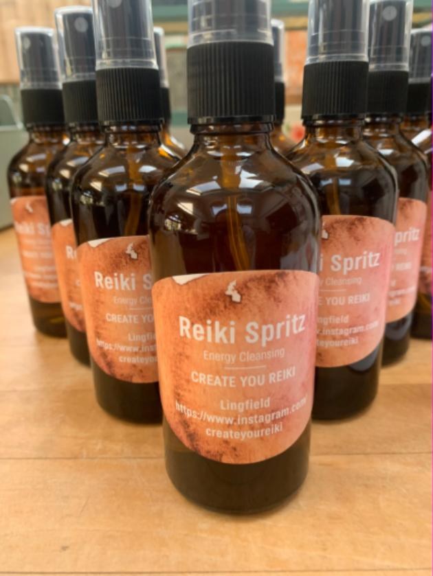 Amber glass bottles of Create You Reiki energy-cleansing spritz with terracotta labels, lined up on a wooden table.