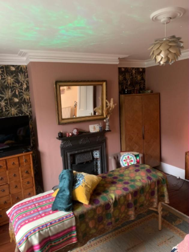 The 1:1 treatment room in Lingfield: a draped treatment couch beside a cast-iron fireplace, with a gilt mirror and warm lamplight.